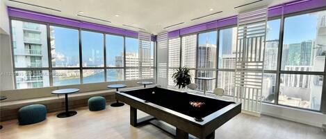 Une table de billard dans une pièce moderne dotée de grandes fenêtres donnant sur la ville.