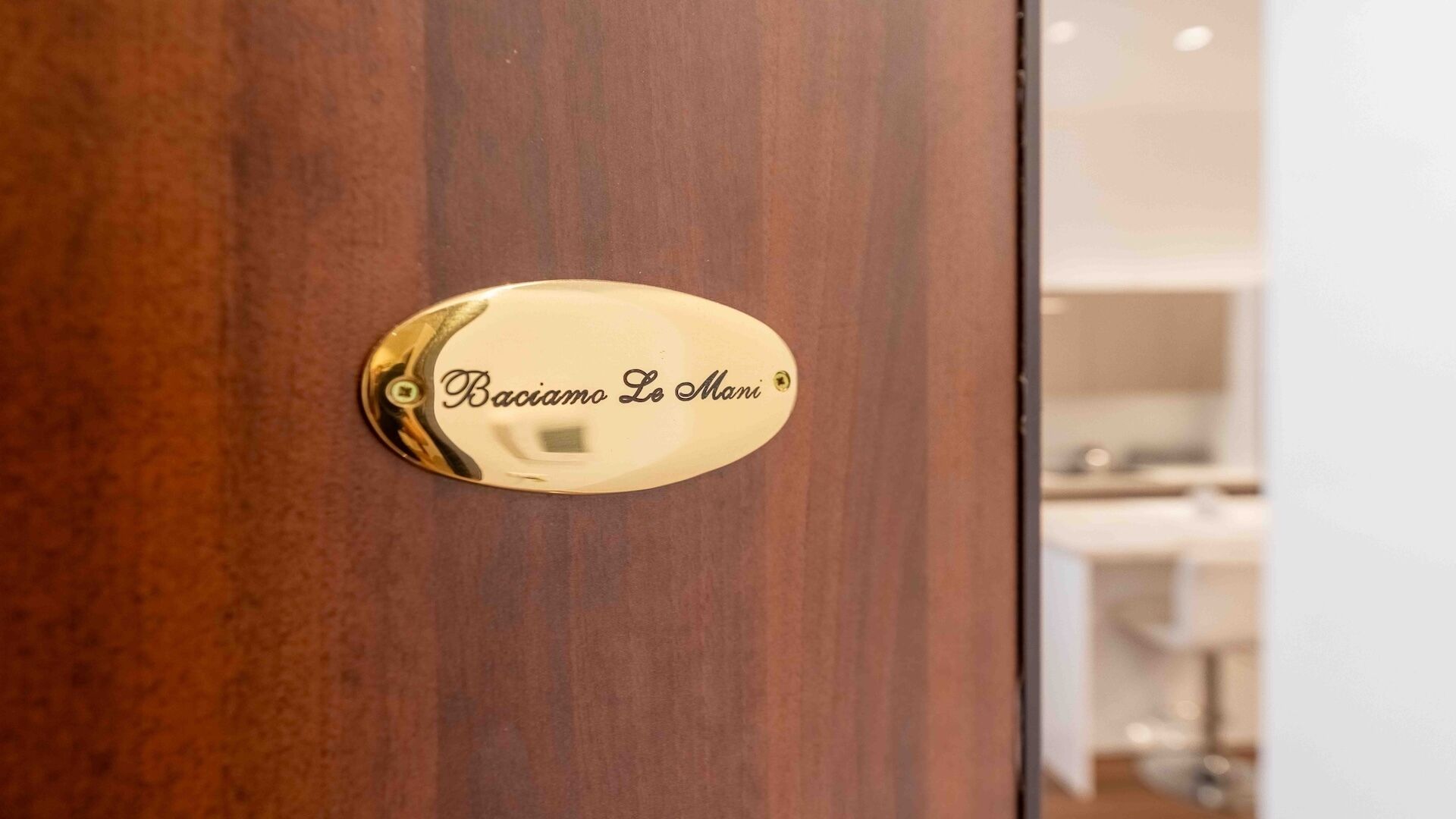 A wooden door with a brass plaque that reads 'Baciamo Le Mani'.