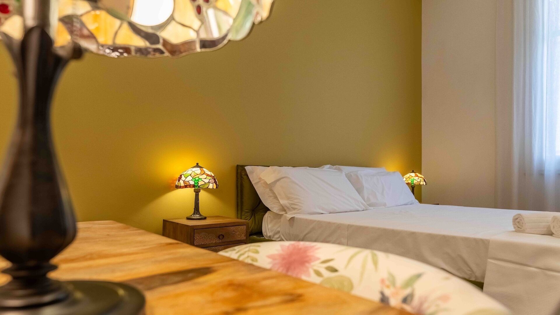 Ett hotellrum med en säng, ett nattduksbord och ett bord med en lampa.