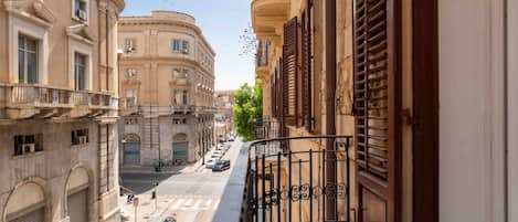 Una calle estrecha flanqueada por edificios, con un balcón a la vista y automóviles estacionados.