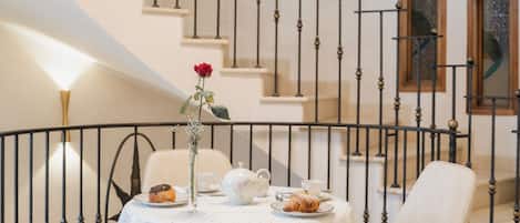 A dining area with a table set for two, a vase with a single flower, and a staircase with a railing.