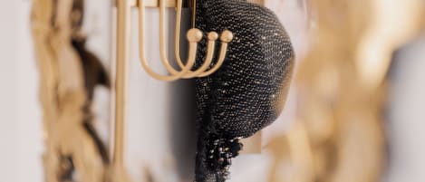 Een sierlijke spiegel met een gouden lijst en een zwart, gestructureerd object eraan.