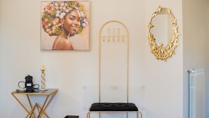 Ein Zimmer mit einem Wandspiegel, einem gerahmten Kunstwerk, einem kleinen Tisch mit Lampe und einer Bank.