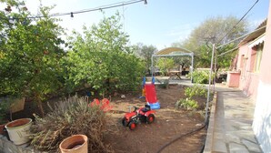 A garden with a red toy tractor, potted plants, and a covered seating area. - Kipseli s Stone House by Frangki (Aegina)