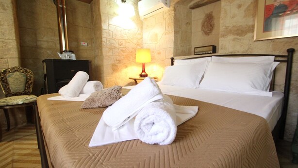 A hotel room with a bed, a wooden chair, a lamp, and a fireplace. - Kipseli s Stone House by Frangki (Aegina)