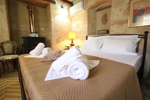 A hotel room with a bed, a wooden chair, a lamp, and a fireplace. - Kipseli s Stone House by Frangki (Aegina)