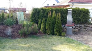 Un jardin aménagé avec un mur en pierre, une variété d’arbustes et une petite construction en pierre.
