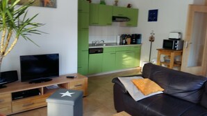 Un salon avec un téléviseur, un canapé avec un coussin, une petite table et une plante.