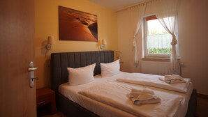 Une chambre d’hôtel avec un grand lit, deux tables de chevet, une lampe fixée au mur et une fenêtre avec des rideaux.