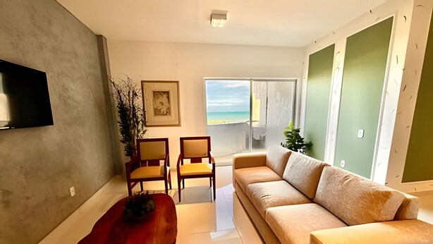 Una sala de estar con un sofá, sillas, una mesa roja, un televisor y vista a la playa.