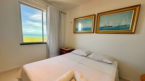 Una habitación de hotel con cama, ventana con vista al mar y dos cuadros enmarcados en la pared.