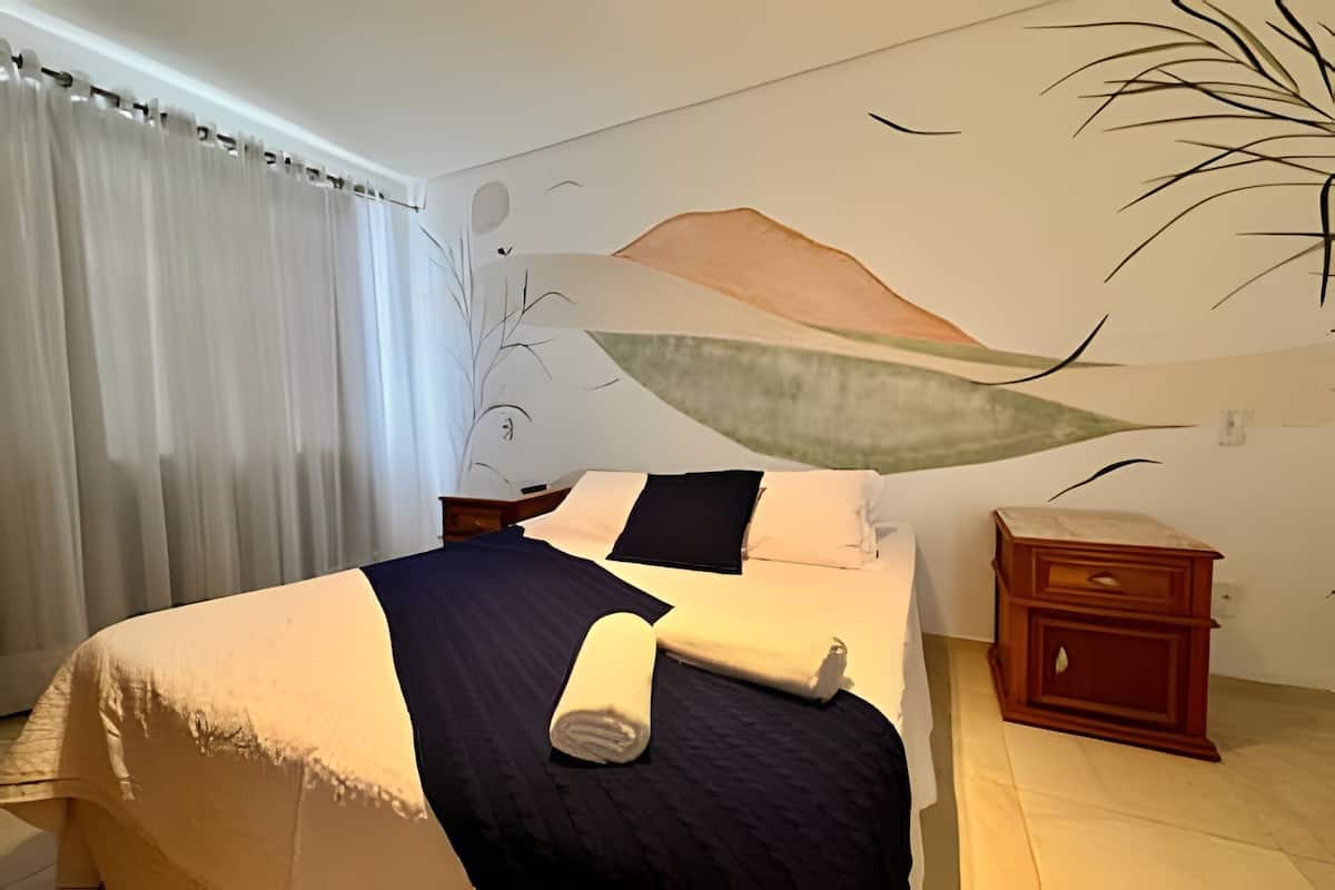 Quarto com cama, mesa de cabeceira e um mural na parede.