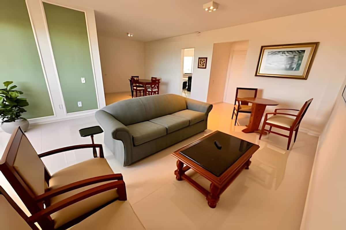 Uma sala de estar com um sofá, duas cadeiras de madeira, uma mesa de centro e uma mesa de jantar com cadeiras.