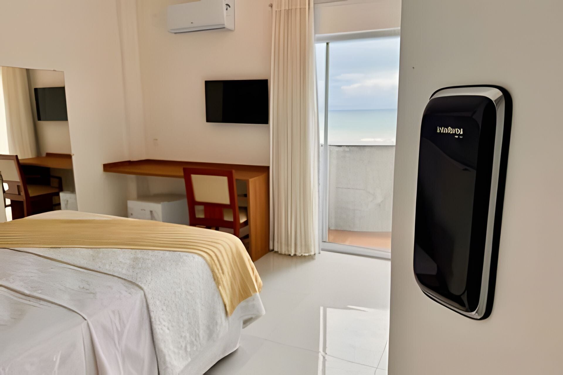 A hotel room with a bed, a desk, a chair, a TV, and a window with a view of the sea.