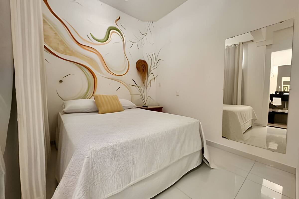 Quarto moderno com cama grande, espelho e uma obra de arte na parede.