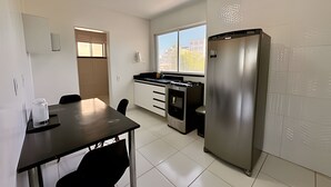 Cocina compacta con refrigerador, ventana y puerta que da a otra habitación.