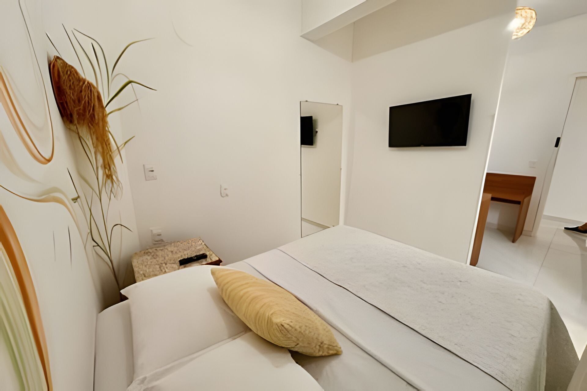 A bedroom with a bed, a flat-screen TV mounted on the wall, and a small table.