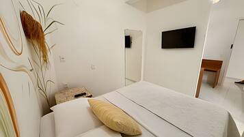 A bedroom with a bed, a flat-screen TV mounted on the wall, and a small table.