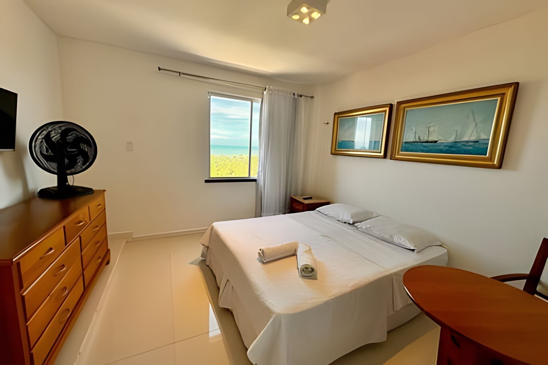 A neatly arranged bedroom with a bed, a desk, a dresser, and two paintings on the wall.