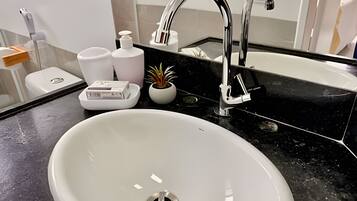 A white bathroom sink with a modern faucet, a soap dispenser, a small potted plant, and a soap dish.