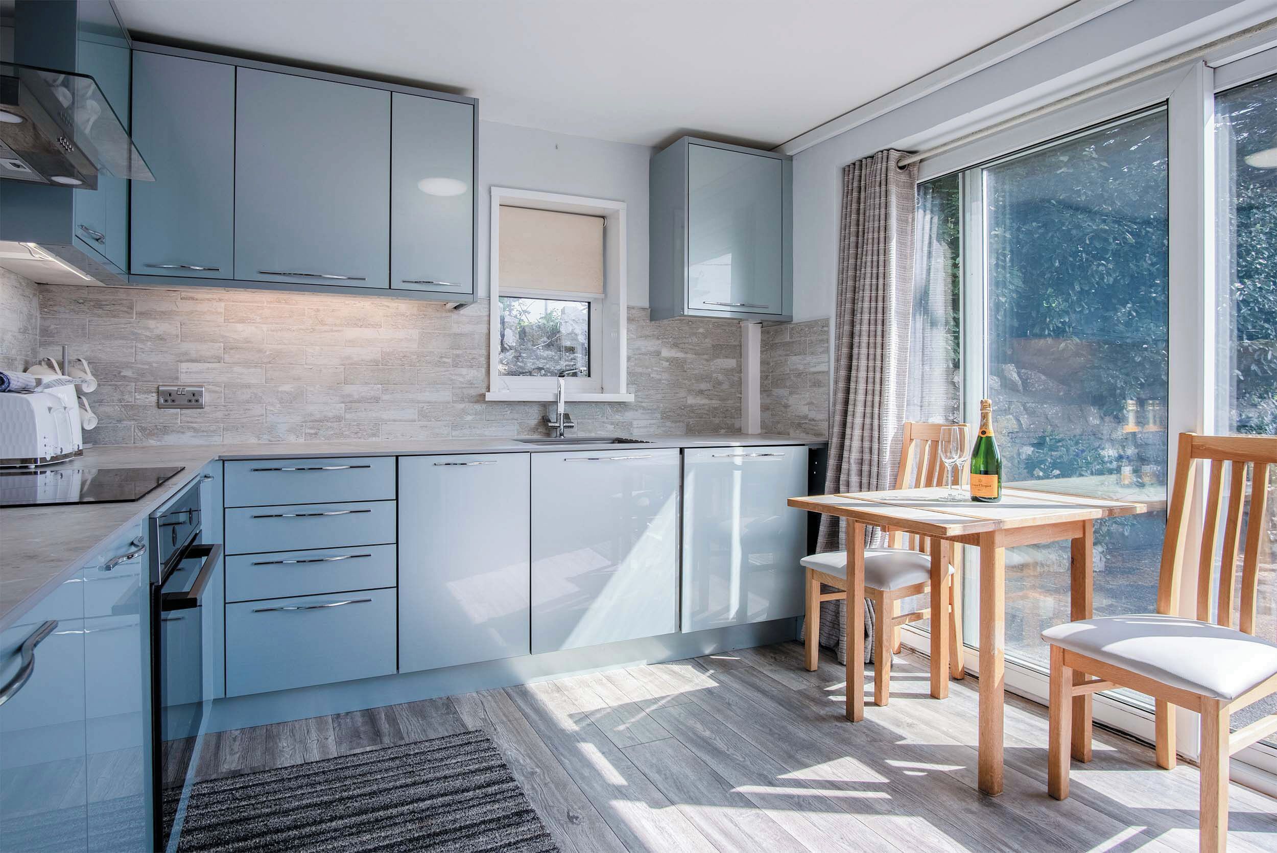 Une cuisine moderne avec des meubles de couleur bleu clair, un lave-vaisselle encastré et un coin repas comprenant une table et des chaises en bois.