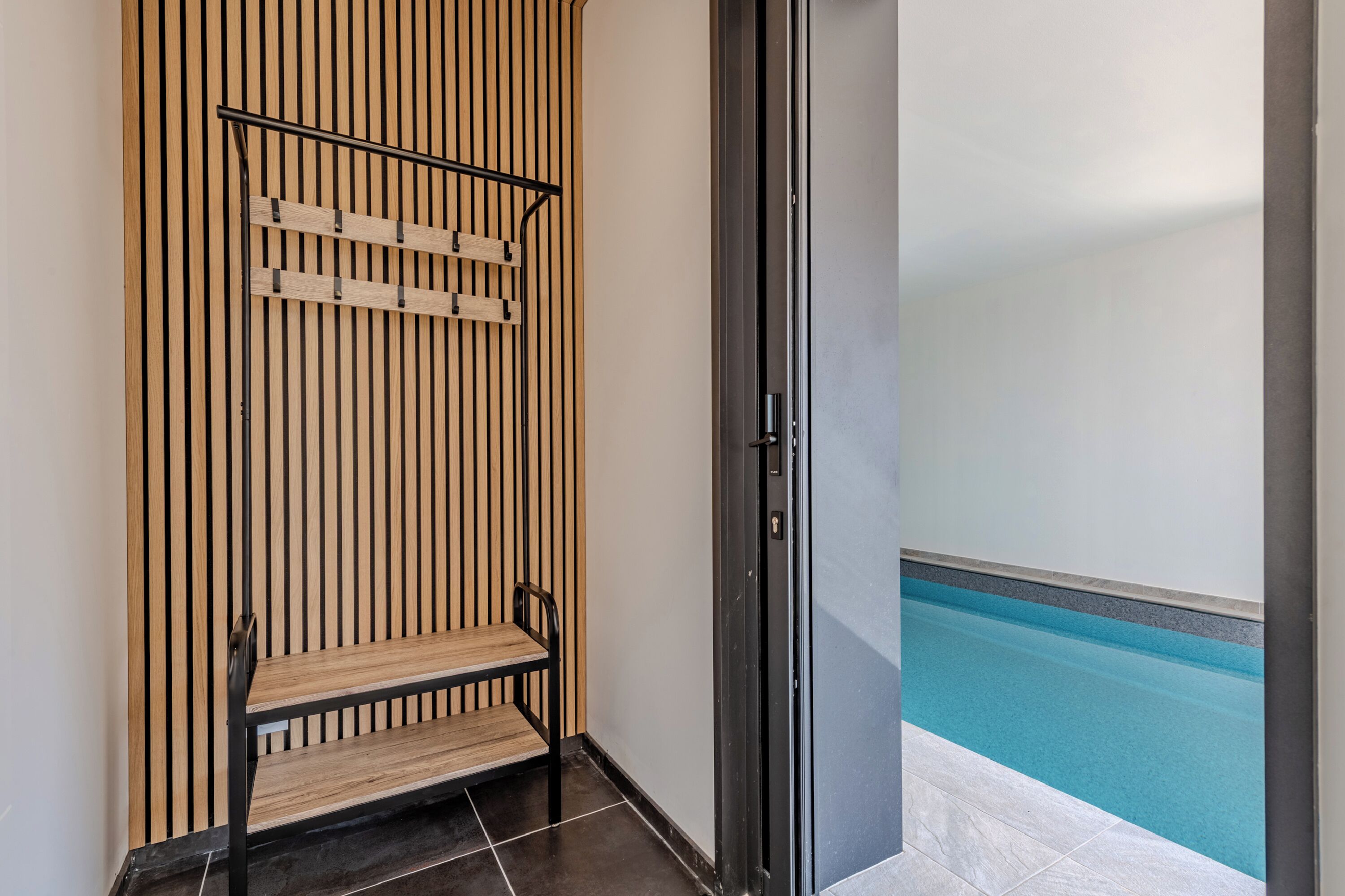 Un baño con pared de listones de madera, un banco y vistas a una piscina.