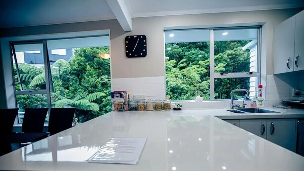 A modern kitchen with a large island, a clock on the wall, and large windows overlooking greenery. - big sale was 158 dollars now from 108 dollars (Wellington)