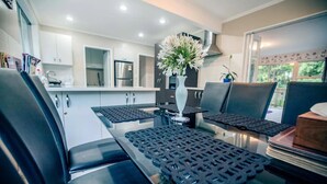 A modern kitchen with white cabinets, a stainless steel refrigerator, and a dining area with black chairs and a glass table. - big sale was 158 dollars now from 108 dollars (Wellington)