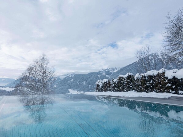 A clear blue infinity pool reflecting snowy mountains and a cloudy sky. - Ideal Apartment With Shared Sauna (Sankt Martin am Tennengebirge)