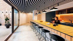 A modern kitchen with a long counter, black bar stools, pendant lighting, and a brick wall visible through the glass door. - Colo Colo. The Smart Hostel Valencia (Valencia)