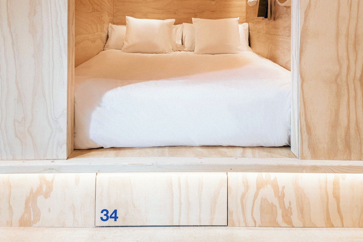 A room with a bed, a nightstand, and a mirror. The room has a wooden ceiling and walls.