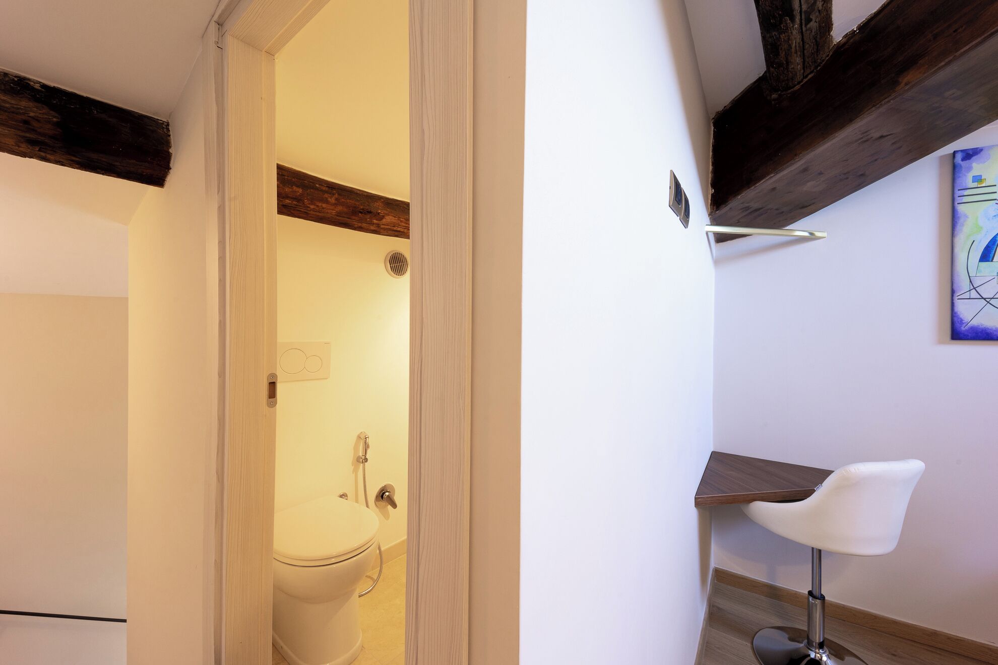 A bathroom with a toilet, shower, and a small table with a chair.