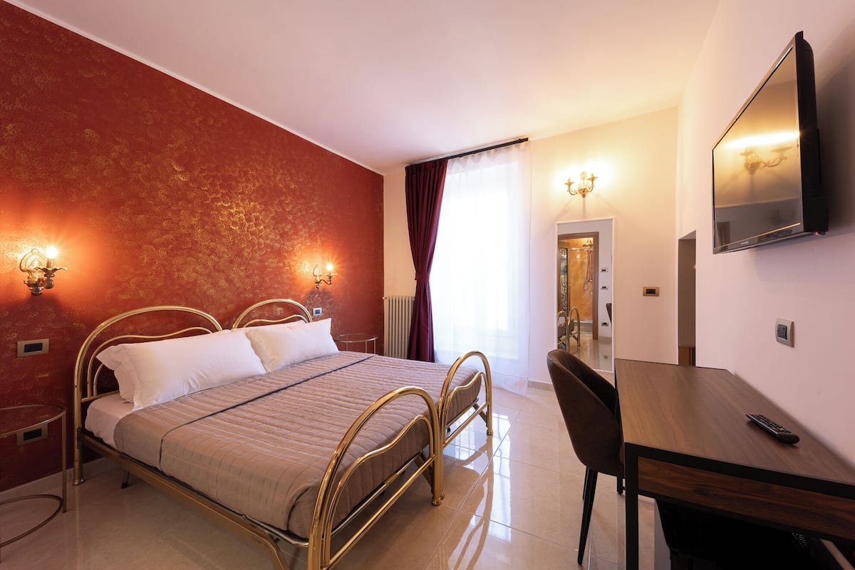 A hotel room with a bed, bedside lamps, a desk, and a television.