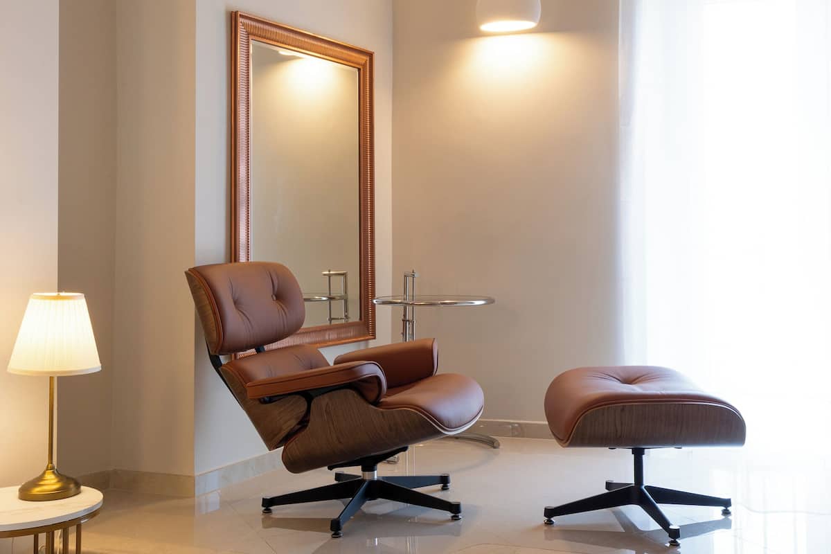 A modern bathroom with a brown leather chair and ottoman, a round mirror, and a small round sink.