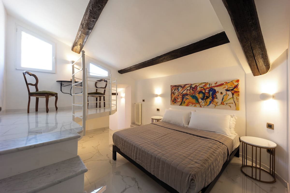 A bedroom with a bed, a chair, a desk, and a painting on the wall.