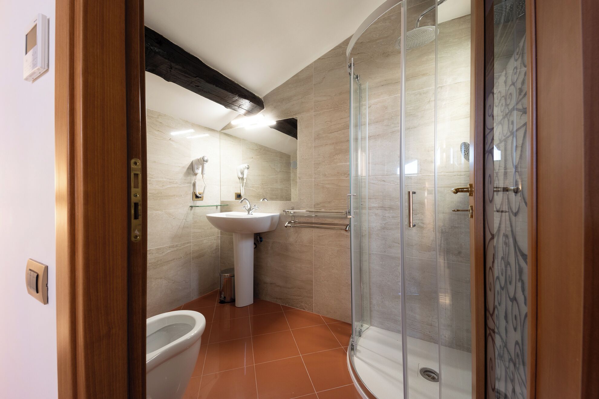 Un bagno con box doccia in vetro, lavabo su piedistallo e water.