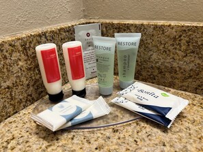 En badeværelsesbordplade med forskellige toiletartikler, herunder skraber, skrøbekrem, shampoo, balsam og body wash.