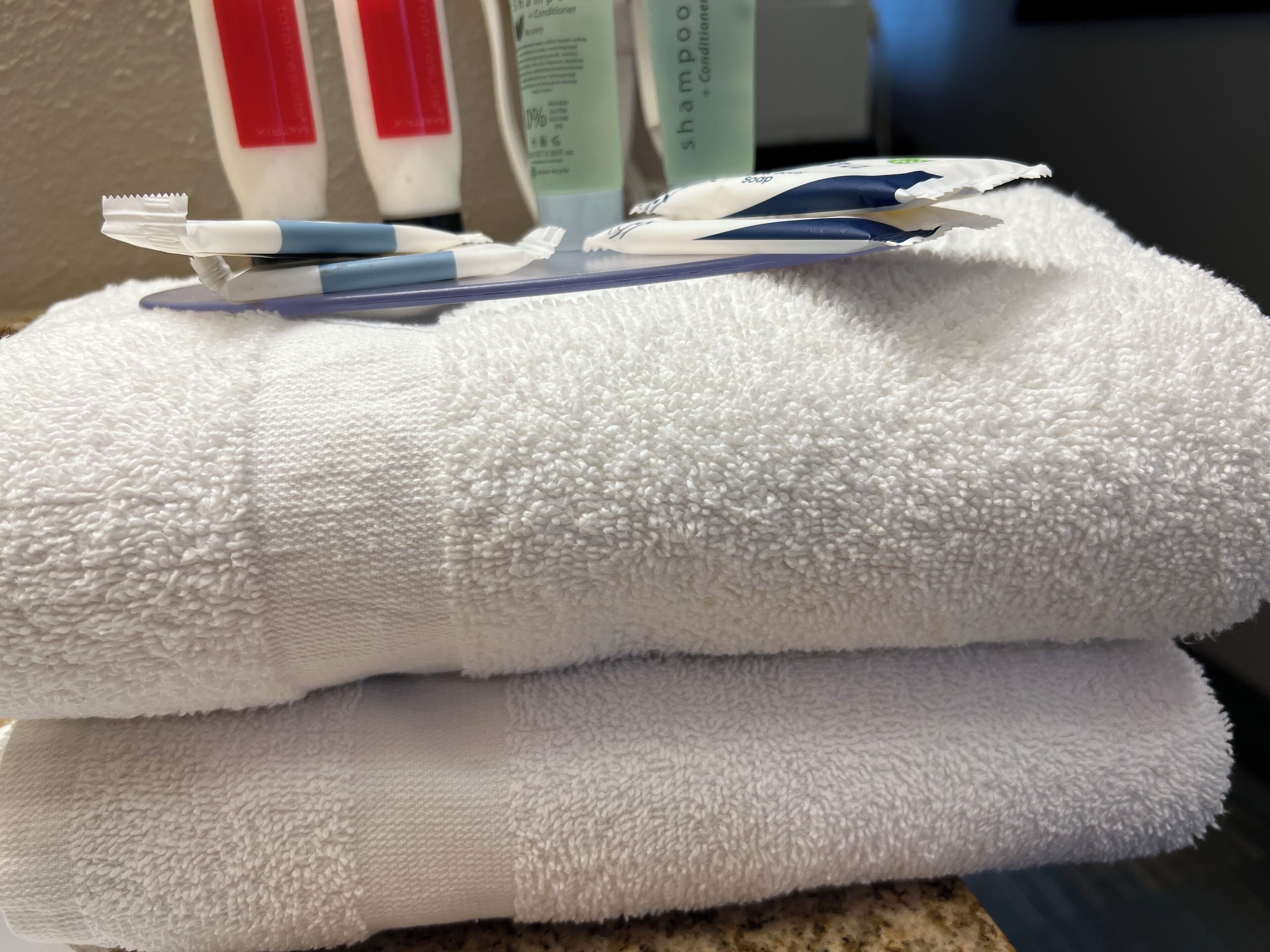 A stack of white towels with a toothbrush and soap bar on top.