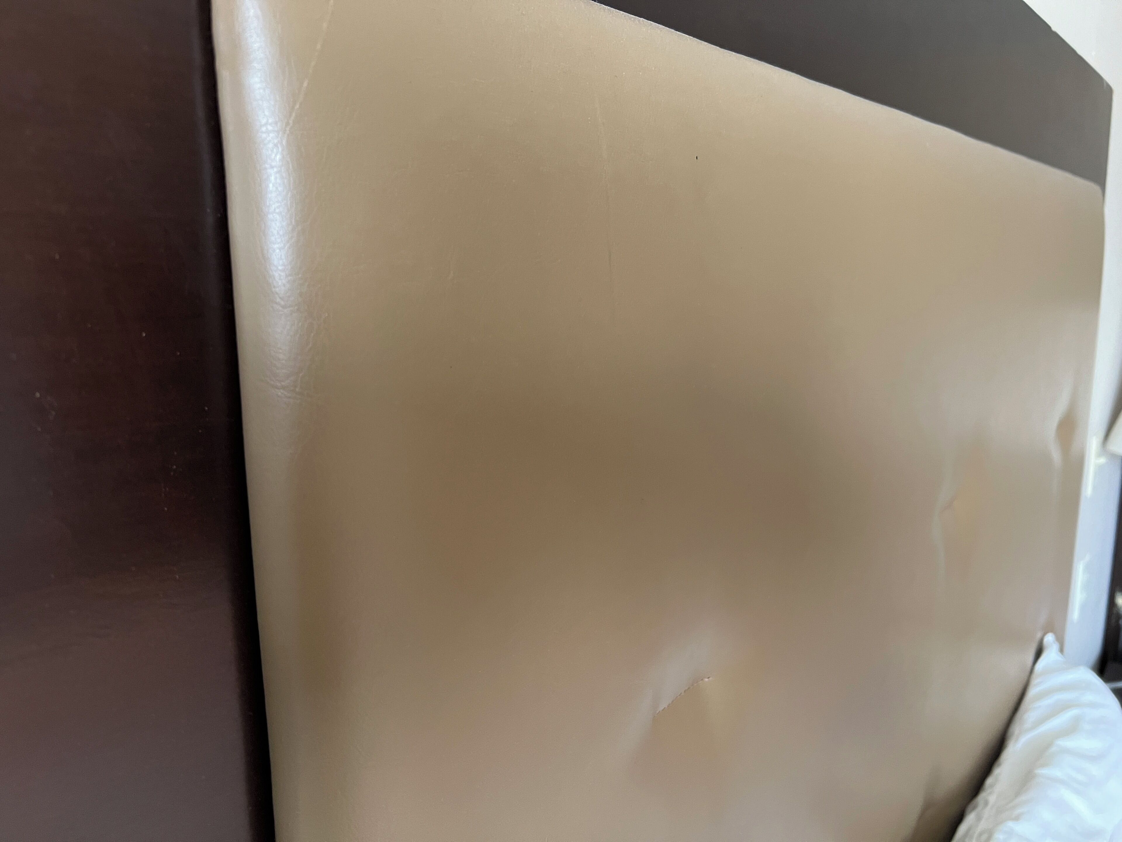 A close-up of a beige upholstered headboard with a visible seam and a dark-colored side panel.