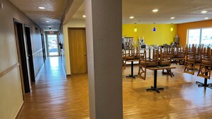 Un couloir doté d’un plancher en bois et d’un mur jaune vif. On y trouve plusieurs tables et chaises disposées dans la pièce.