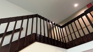 Un escalier en bois, doté d’une rampe, mène à un palier où se trouve un luminaire.