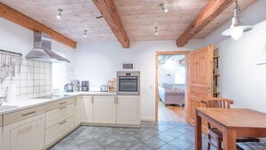 Une cuisine avec des meubles blancs, un plafond en bois et un coin repas comprenant une table et des chaises.