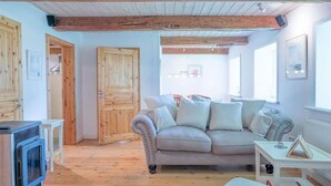 Un salon chaleureux avec un canapé beige, des poutres en bois, une table blanche et un four encastré.