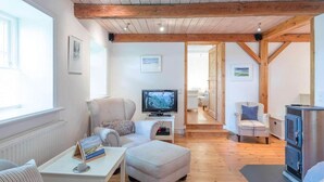 Un salon confortable avec une télévision, un canapé, un fauteuil et une table sur laquelle se trouvent un livre et une tasse.