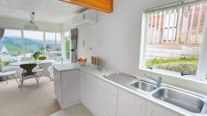 Una cocina moderna con armarios blancos, un lavamanos doble y un amplio ventanal con vistas a una colina.