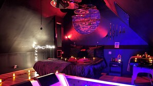 Una habitación tenuemente iluminada con una cama, una mesa de masajes y un aplique circular en la pared.