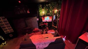 Un espace salon confortable avec un canapé, un téléviseur à écran plat et un mur décoratif agrémenté de plantes.