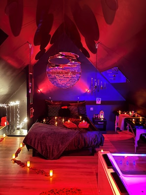 A room with a bed, a massage table, and a large circular wall decoration. - La Sainteny Touch - Erotic Room (Terre-et-Marais)