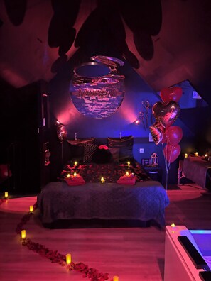 A dimly lit room with a bed, candles, and heart-shaped balloons.