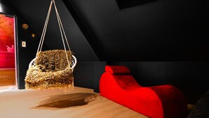 Un interior moderno con un sillón colgante hecho de materiales naturales, un banco acolchado rojo y un suelo de madera.